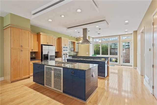 kitchen with dark stone counters, light wood-style floors, island exhaust hood, a large island, and stainless steel appliances