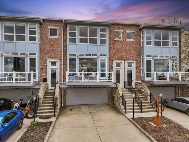 townhome / multi-family property featuring a garage, brick siding, stairs, and concrete driveway