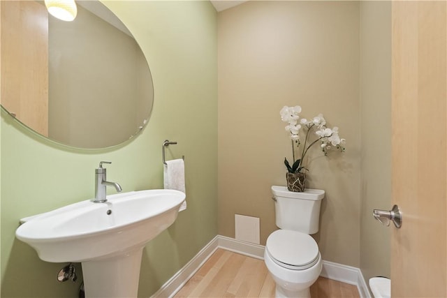 half bathroom with baseboards, wood finished floors, a sink, and toilet