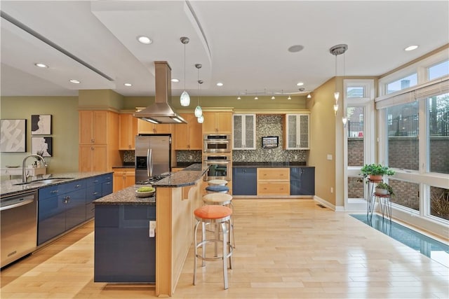 kitchen with stainless steel appliances, light brown cabinetry, a sink, a kitchen bar, and island range hood