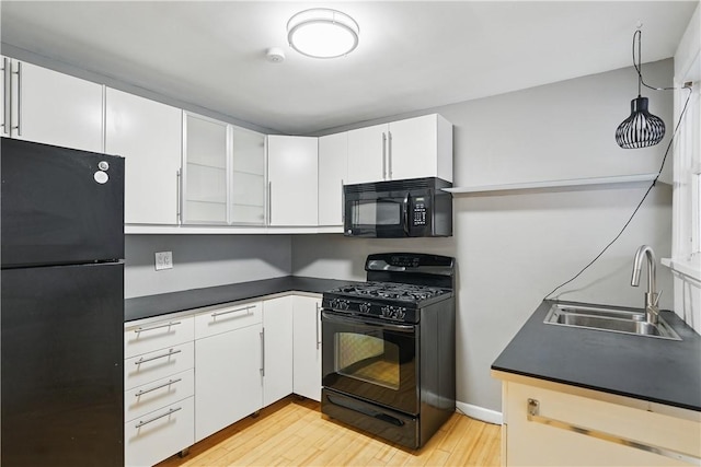 kitchen featuring white cabinetry, light wood finished floors, a sink, and black appliances