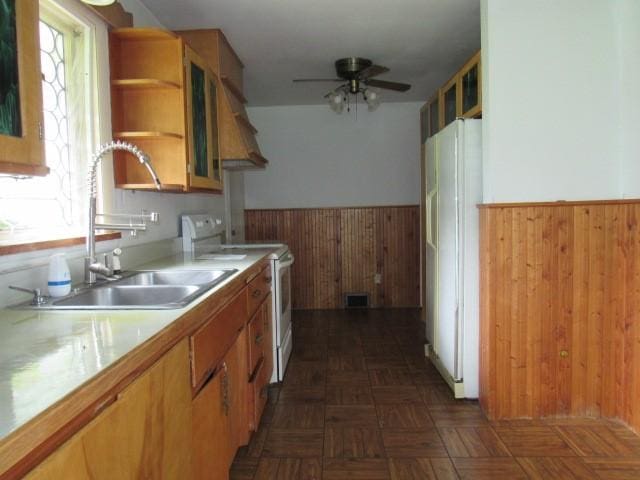 kitchen with white appliances, wood walls, a sink, a wainscoted wall, and light countertops