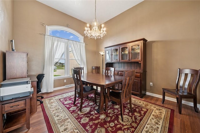 dining space with wood finished floors, a towering ceiling, baseboards, and a notable chandelier