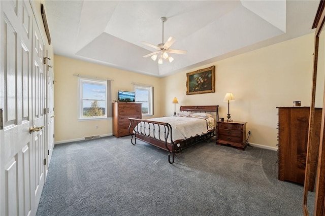 carpeted bedroom with baseboards, a ceiling fan, a tray ceiling, and visible vents