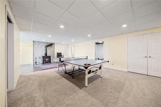 playroom with a paneled ceiling, baseboards, carpet, and a wood stove