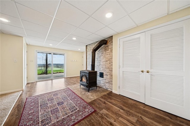 unfurnished living room featuring a paneled ceiling, dark wood-style flooring, baseboards, recessed lighting, and a wood stove