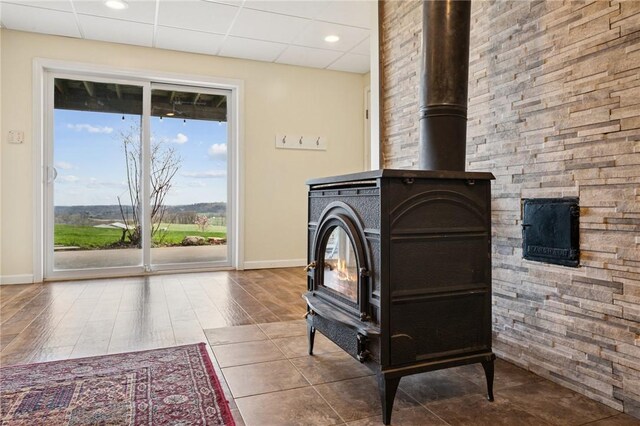 room details featuring wood finished floors, a paneled ceiling, baseboards, and a wood stove