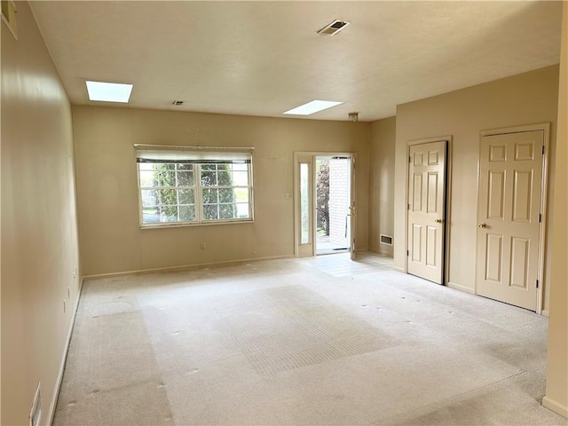 spare room with a skylight, light colored carpet, and baseboards