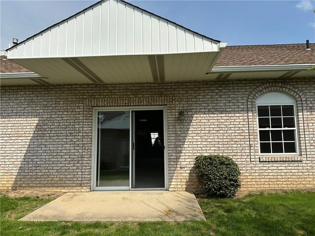 property entrance with brick siding, a shingled roof, and a patio area