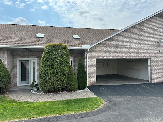 view of side of home featuring brick siding, asphalt driveway, a garage, and roof with shingles