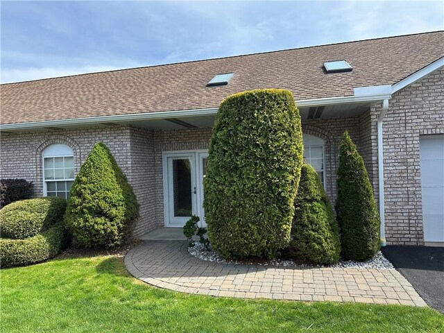 view of exterior entry with brick siding and a shingled roof