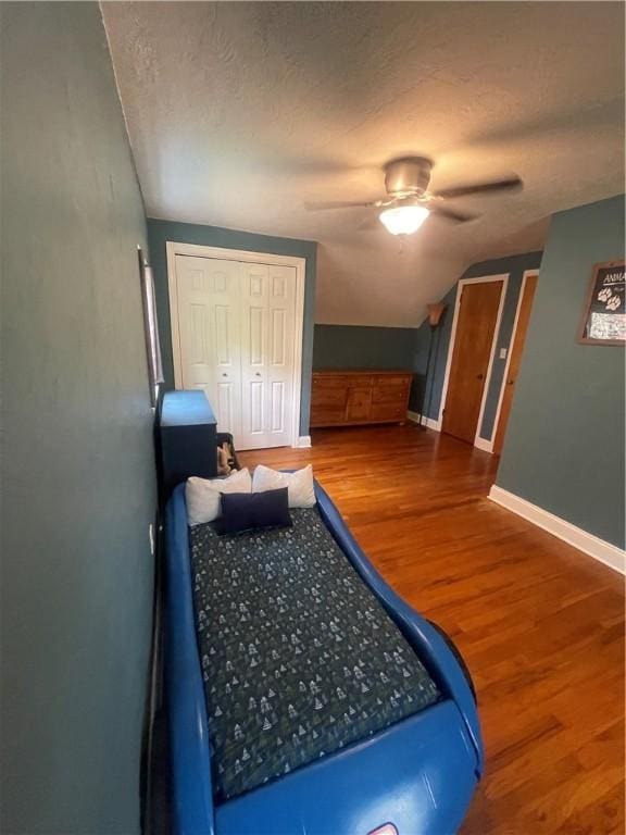 bedroom featuring vaulted ceiling, baseboards, wood finished floors, a closet, and ceiling fan