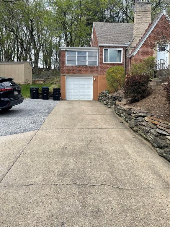 view of side of home featuring roof with shingles, a chimney, concrete driveway, brick siding, and a garage