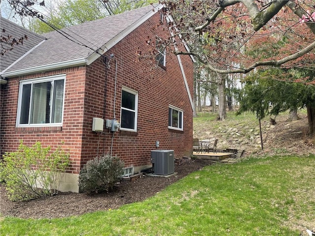 view of side of property featuring central air condition unit, brick siding, roof with shingles, and a lawn