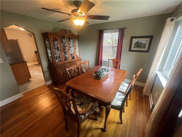 dining area with arched walkways, light wood finished floors, a ceiling fan, and baseboards
