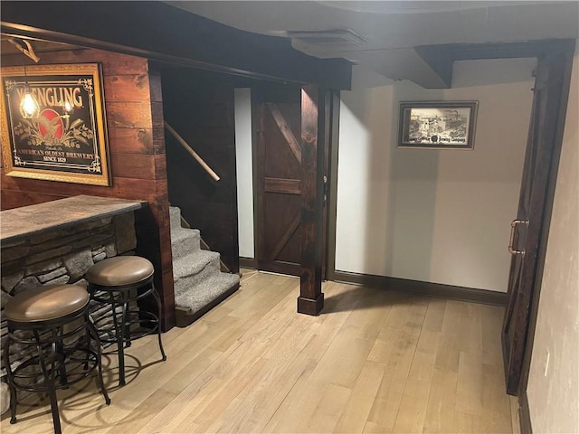 bar featuring wood finished floors, a bar, baseboards, and stairway