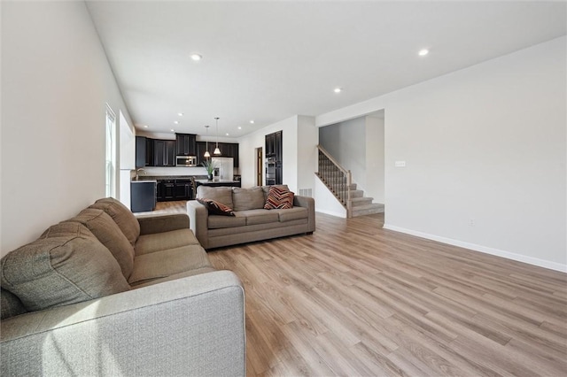 living area with stairway, baseboards, light wood finished floors, and recessed lighting