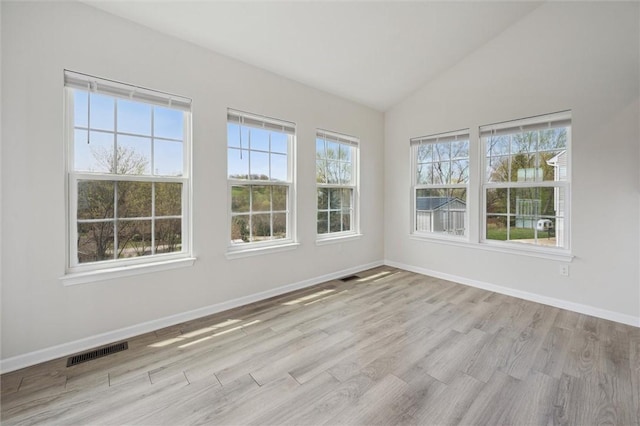 spare room with vaulted ceiling, wood finished floors, visible vents, and baseboards