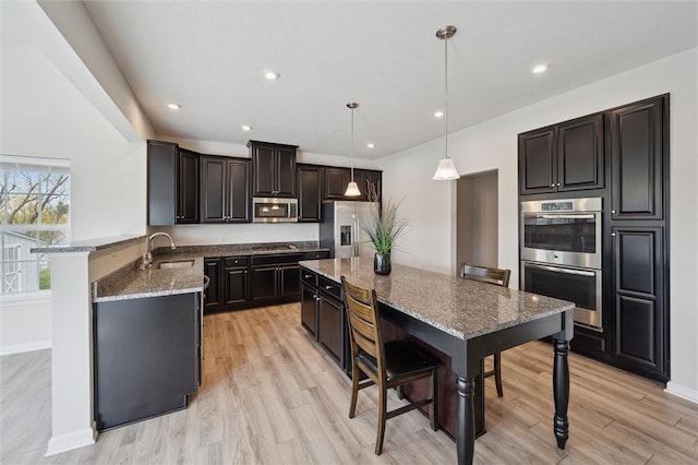 kitchen with light wood-style flooring, a sink, stone countertops, a kitchen island, and appliances with stainless steel finishes