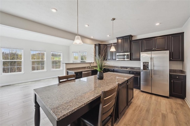 kitchen with dark brown cabinets, light stone countertops, stainless steel appliances, and light wood finished floors