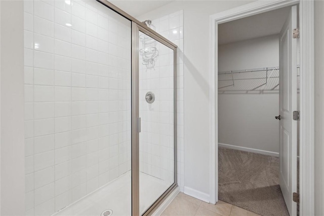 bathroom featuring a walk in closet, a shower stall, tile patterned floors, and baseboards