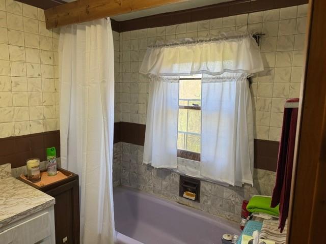 full bath featuring tile walls and shower / bath combo with shower curtain