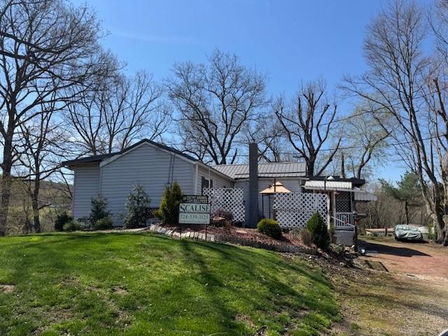back of house with a chimney, a yard, and metal roof