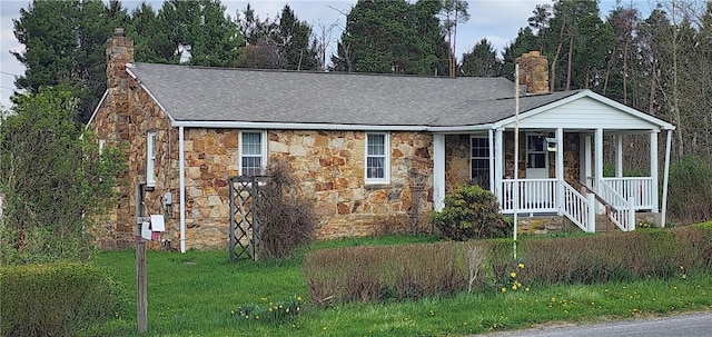 view of front of home featuring stone siding, covered porch, a chimney, and roof with shingles