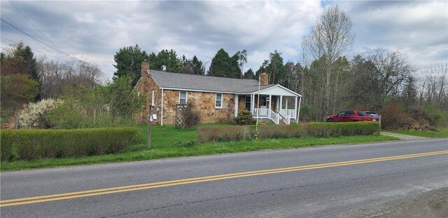 ranch-style house with stone siding, a porch, a chimney, and a front yard