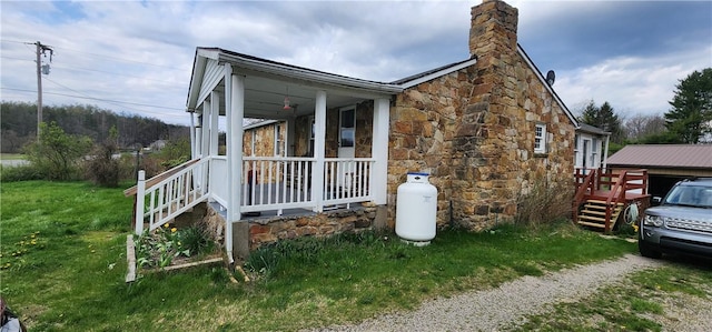 view of side of property with a yard, a chimney, stone siding, and covered porch