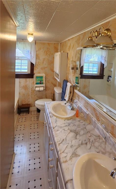 full bath featuring toilet, a sink, double vanity, and baseboards