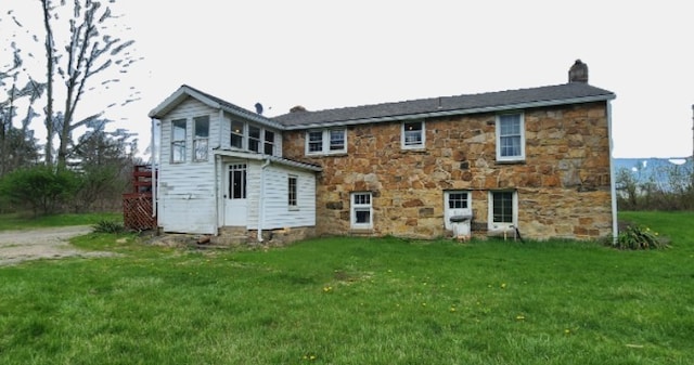 back of house with stone siding, a lawn, and a chimney