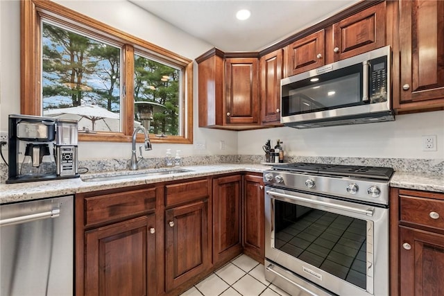 kitchen with appliances with stainless steel finishes, light stone countertops, a sink, and light tile patterned floors