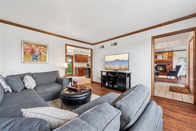 living room featuring crown molding, a brick fireplace, wood finished floors, and visible vents