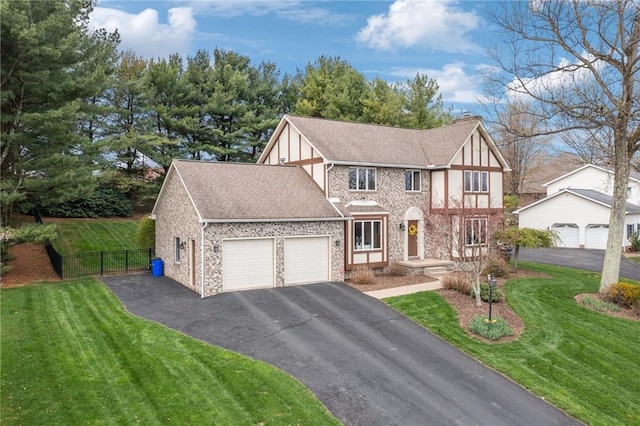 tudor-style house featuring fence, a front lawn, driveway, stone siding, and a garage