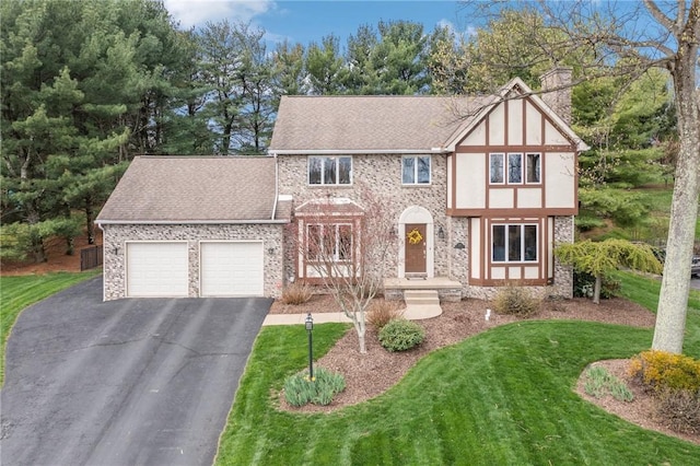 tudor house featuring a chimney, aphalt driveway, a shingled roof, a front lawn, and a garage