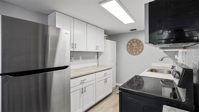 kitchen with white cabinets, freestanding refrigerator, light wood-style floors, and a sink
