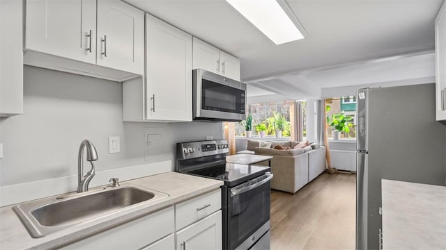 kitchen with light countertops, a sink, light wood-style flooring, appliances with stainless steel finishes, and white cabinetry