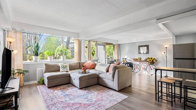 living room featuring beamed ceiling, baseboards, and wood finished floors