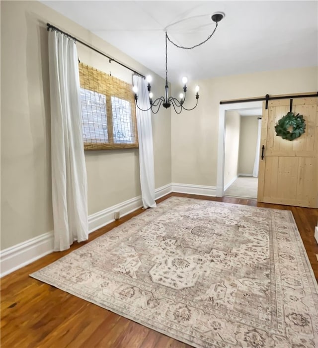 unfurnished dining area with baseboards, wood finished floors, an inviting chandelier, and a barn door