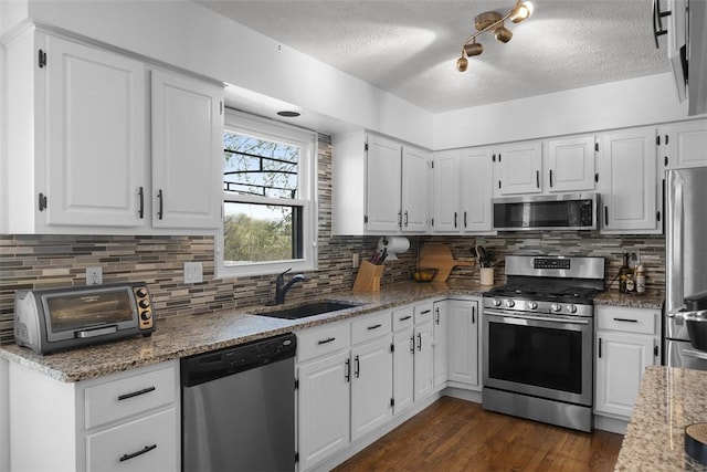 kitchen with stainless steel appliances, a sink, a textured ceiling, dark wood-style floors, and decorative backsplash
