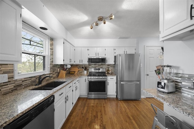kitchen with appliances with stainless steel finishes, a sink, a textured ceiling, tasteful backsplash, and white cabinets
