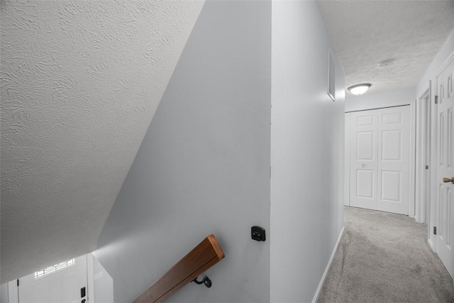 corridor featuring a textured ceiling, carpet, and baseboards