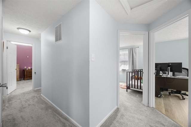 corridor featuring carpet floors, a desk, a textured ceiling, and baseboards