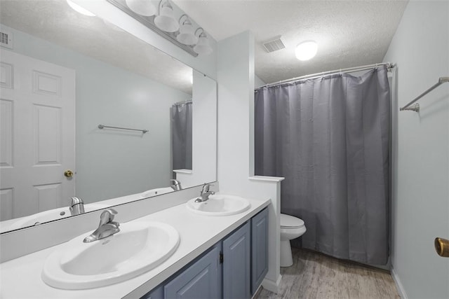 full bathroom featuring wood finished floors, double vanity, a textured ceiling, toilet, and a shower with curtain