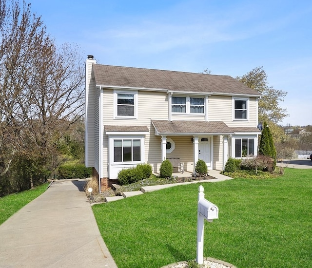 traditional home with a chimney, a porch, a front lawn, and driveway
