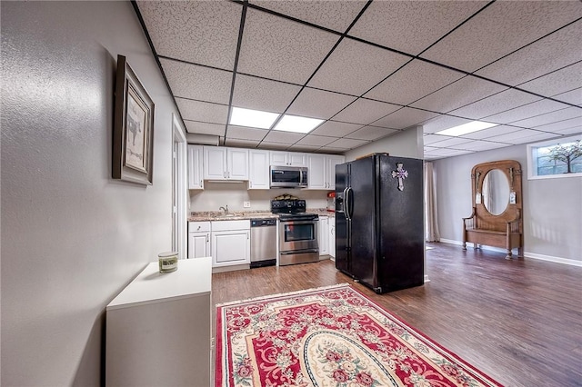 kitchen featuring stainless steel appliances, dark wood-style flooring, white cabinets, a sink, and a drop ceiling