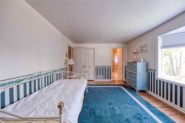 bedroom with wood finished floors, wallpapered walls, wainscoting, and a closet