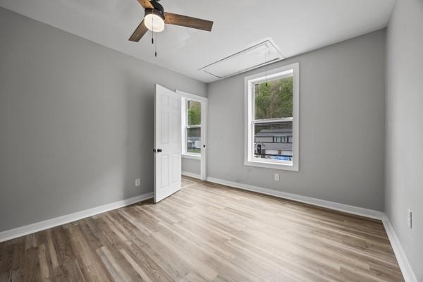 empty room with attic access, ceiling fan, wood finished floors, and baseboards
