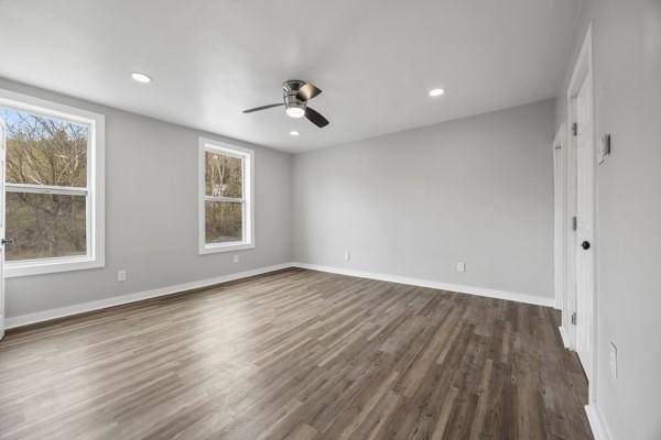 unfurnished room featuring a wealth of natural light, a ceiling fan, dark wood finished floors, and baseboards